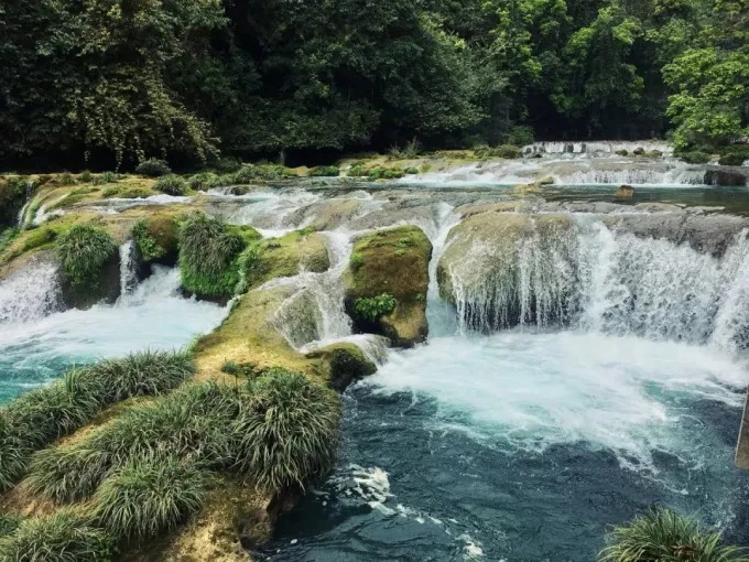 Cascada escalonada junto a una pasarela de madera en Xiaoqikong
