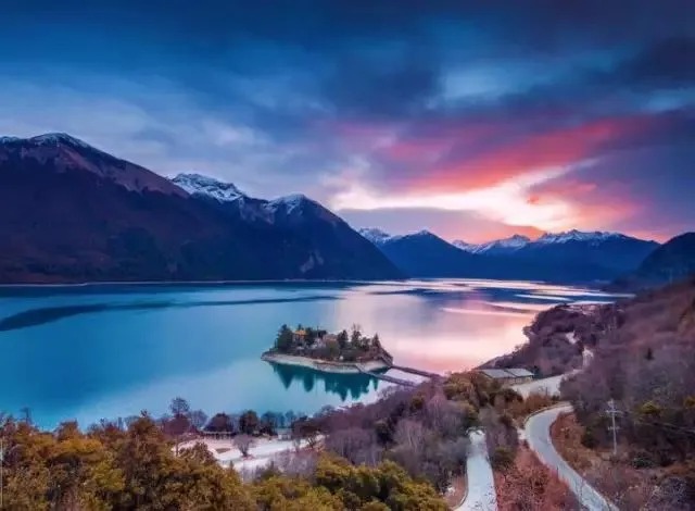 Der See Basum Tso mit bewaldeten Hängen und Schnee im Hintergrund