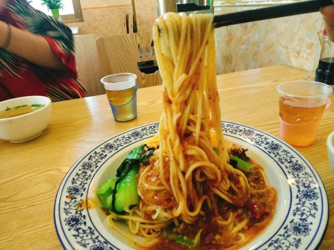 Un cuenco de fideos mezclados con salsa oscura, patata y verduras