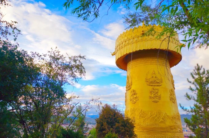 The large golden prayer wheel rising beside trees in Shangri-La