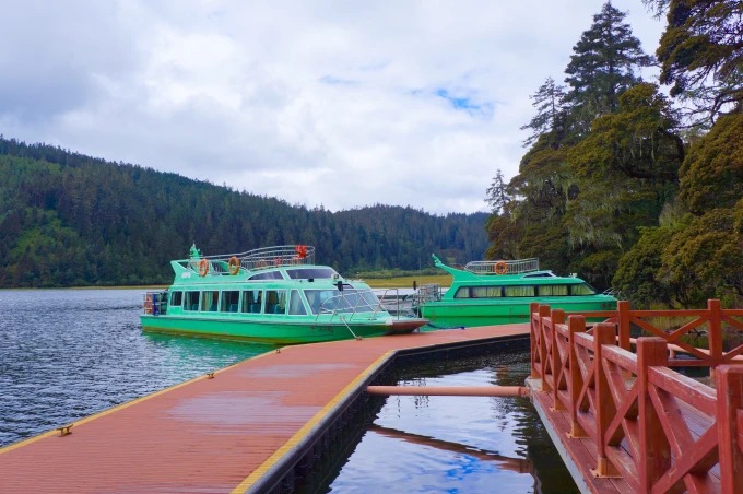 Green passenger boats at a wooden jetty on a forest-edged lake