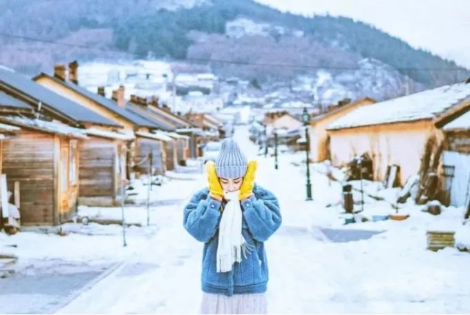 Una visitante en una calle nevada de casas de madera en Hengdaohezi