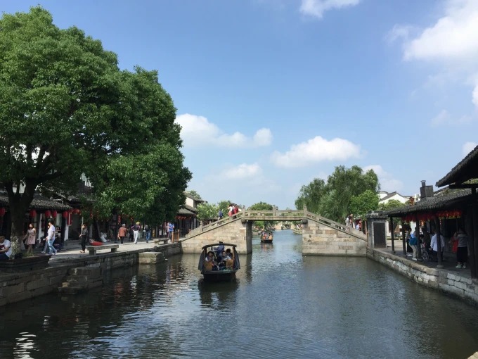 Ein Fahrgastboot nähert sich einer Steinbrücke in Xitang