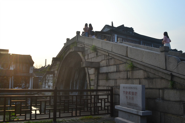 Besucher überqueren eine steinerne Bogenbrücke in Xitang