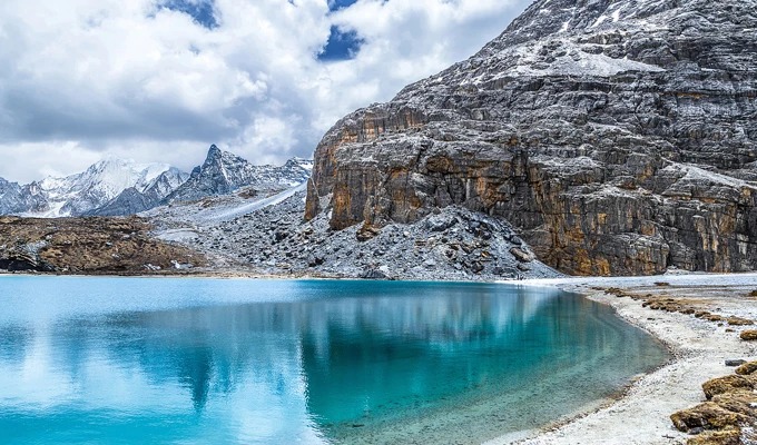 Ein blaugrüner Hochlandsee unter schneebedeckten Felswänden in Yading